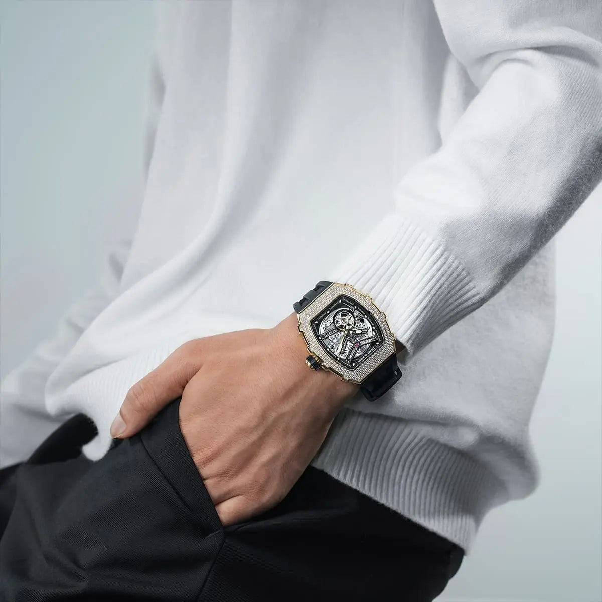 A man wearing a TSAR BOMBA tonneau skeleton watch with a black strap and cubic zirconia diamond bezel.