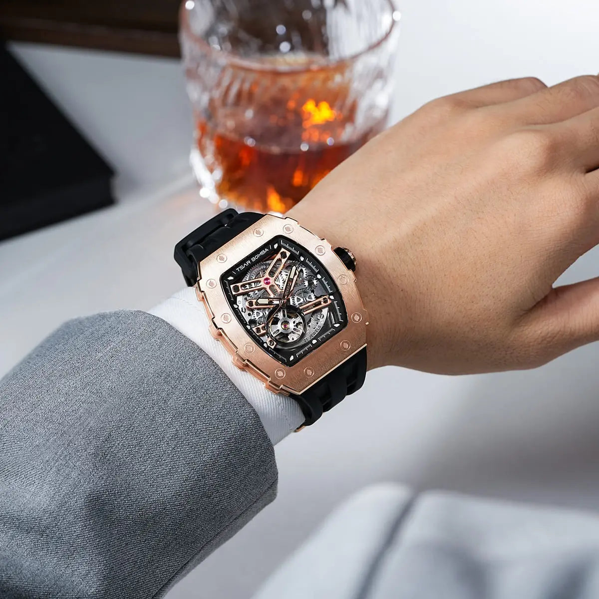TSAR BOMBA TB8208A rose gold-tone tonneau skeleton watch with a black strap, worn with a grey suit and white shirt