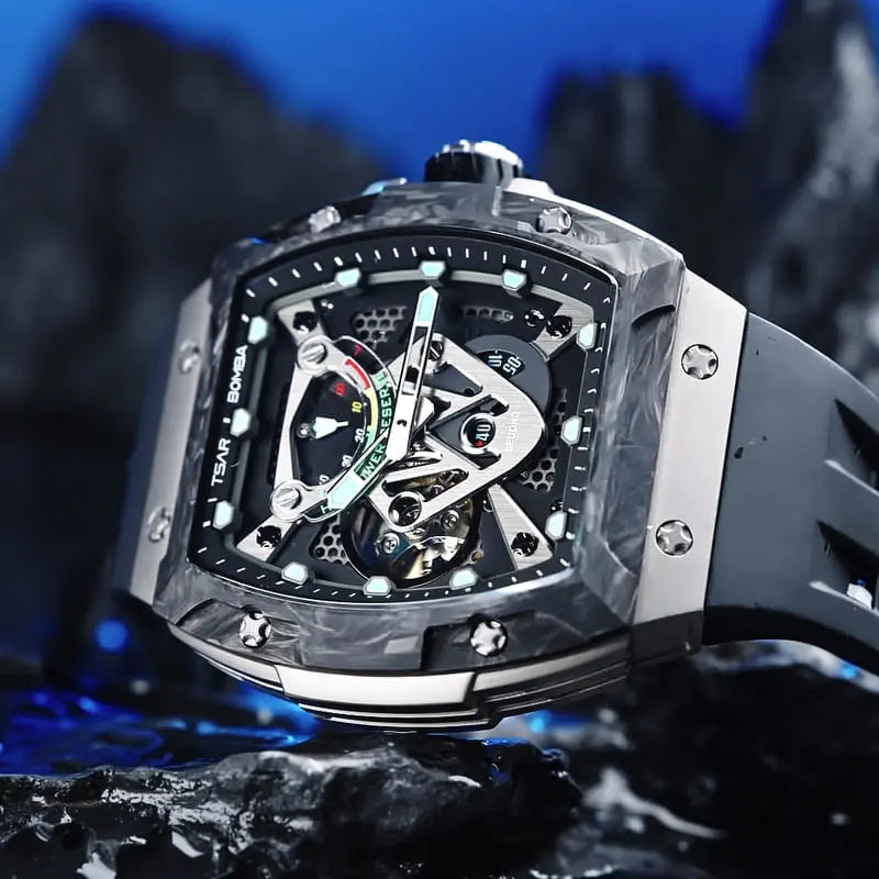 TSAR BOMBA tonneau skeleton watch with a dark carbon fiber bezel, silver side panels, black strap, and luminous turquoise dial accents, displayed on a rock against a dramatic blue background.