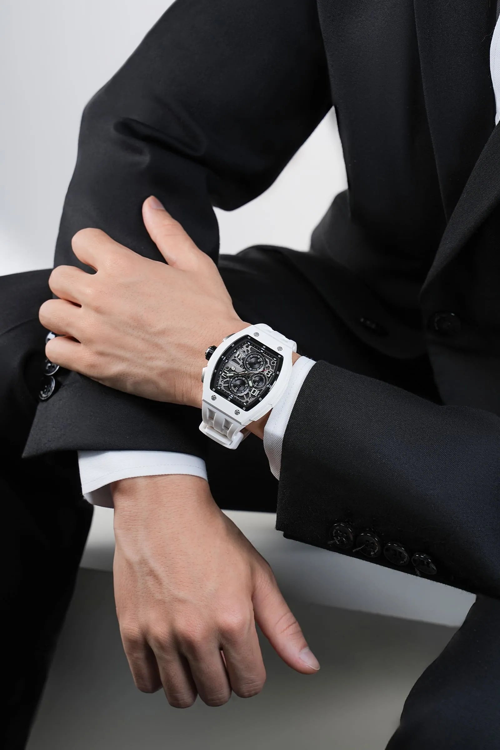 In the photo, a male model seated in a chair wears the TB8224B watch on his wrist, with the dial facing the viewer; the watch features an white strap and a white bezel. This highlights the stylish look of this barrel-shaped watch when worn