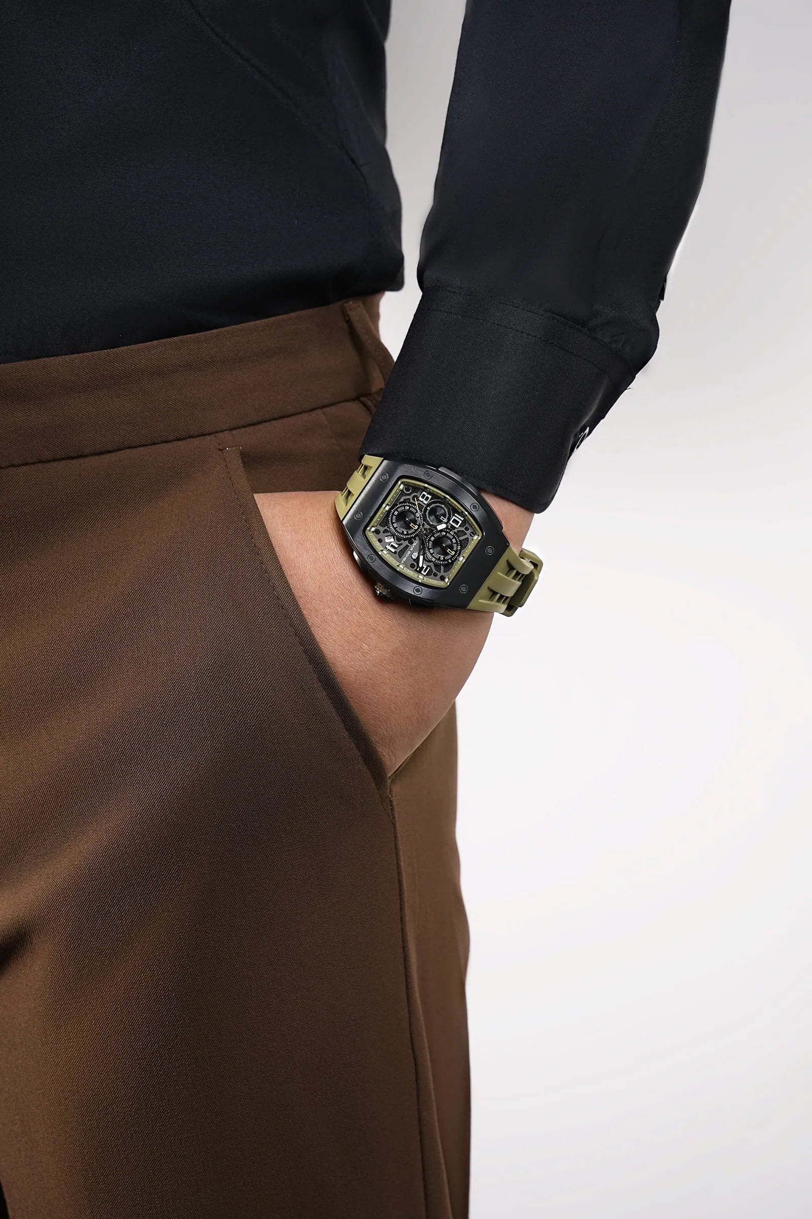 In the photo, a male model seated in a chair wears the TB8224Q watch on his wrist, with the dial facing the viewer; the watch features an olive-green strap and a black bezel. This highlights the stylish look of this barrel-shaped watch when worn.